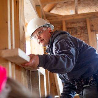 A woman holding a two-by-four on a construction site. 