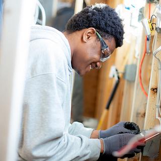 A young man works on electrical in a wall. 