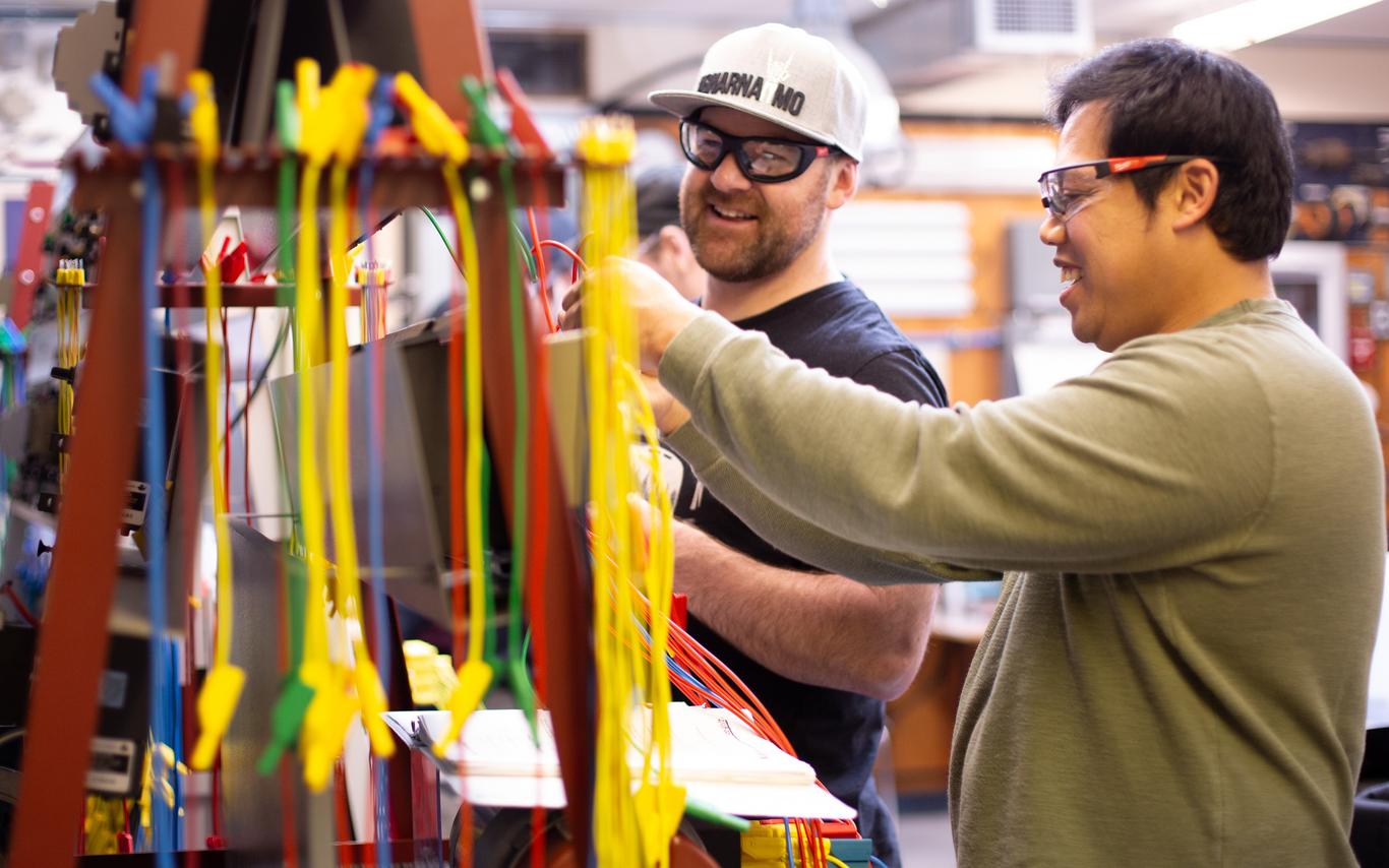 Two men smiling as they work in an electrical shop