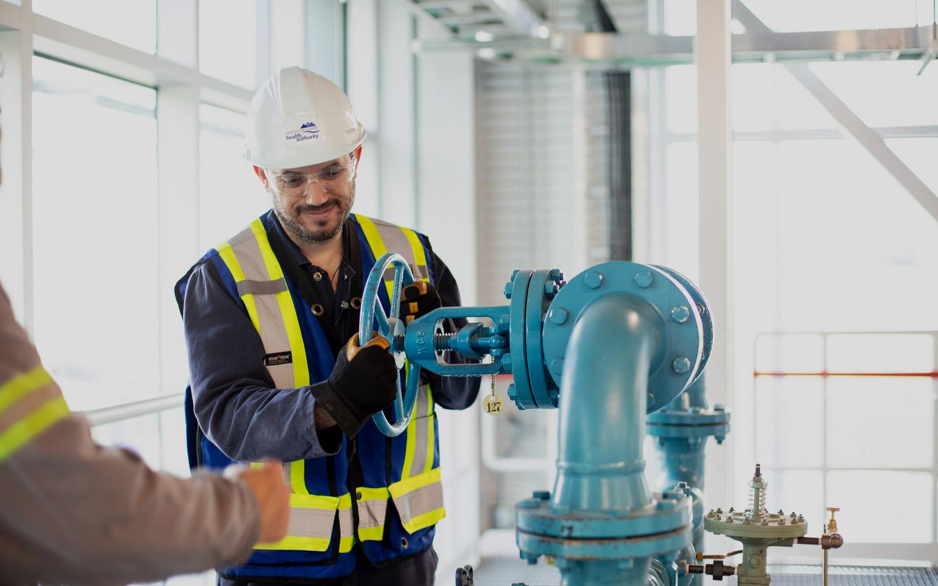 A man in safety gear working on large pipes. 