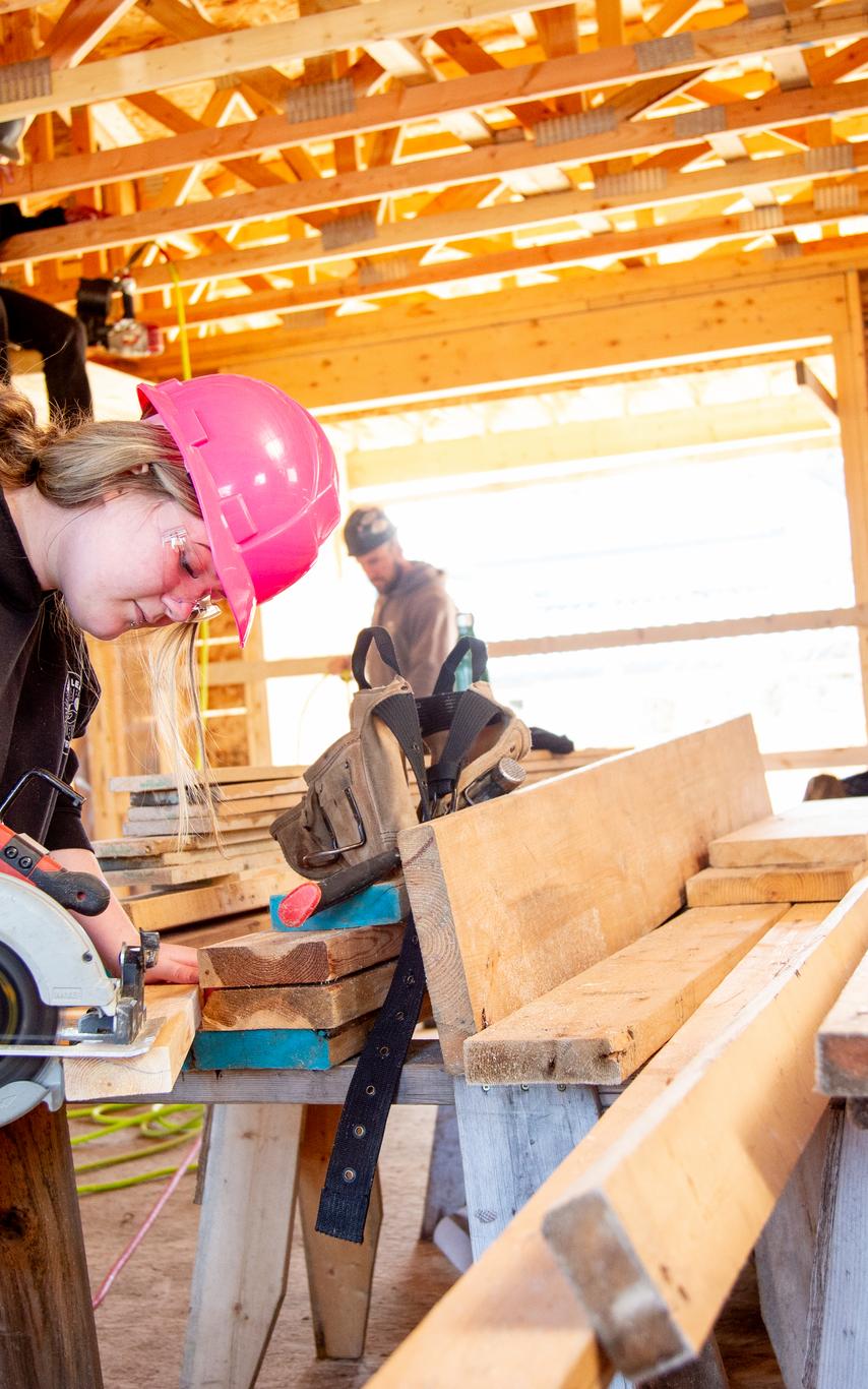 A carpentry student is working on site building a house. She is cutting wood using a circular saw.